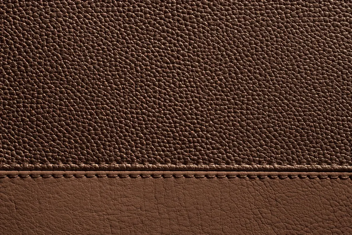 Close-up of full-grain leather surface showing natural pebbled grain pattern and hand-stitched seam — the defining texture of premium cowhide used in wholesale handbag manufacturing