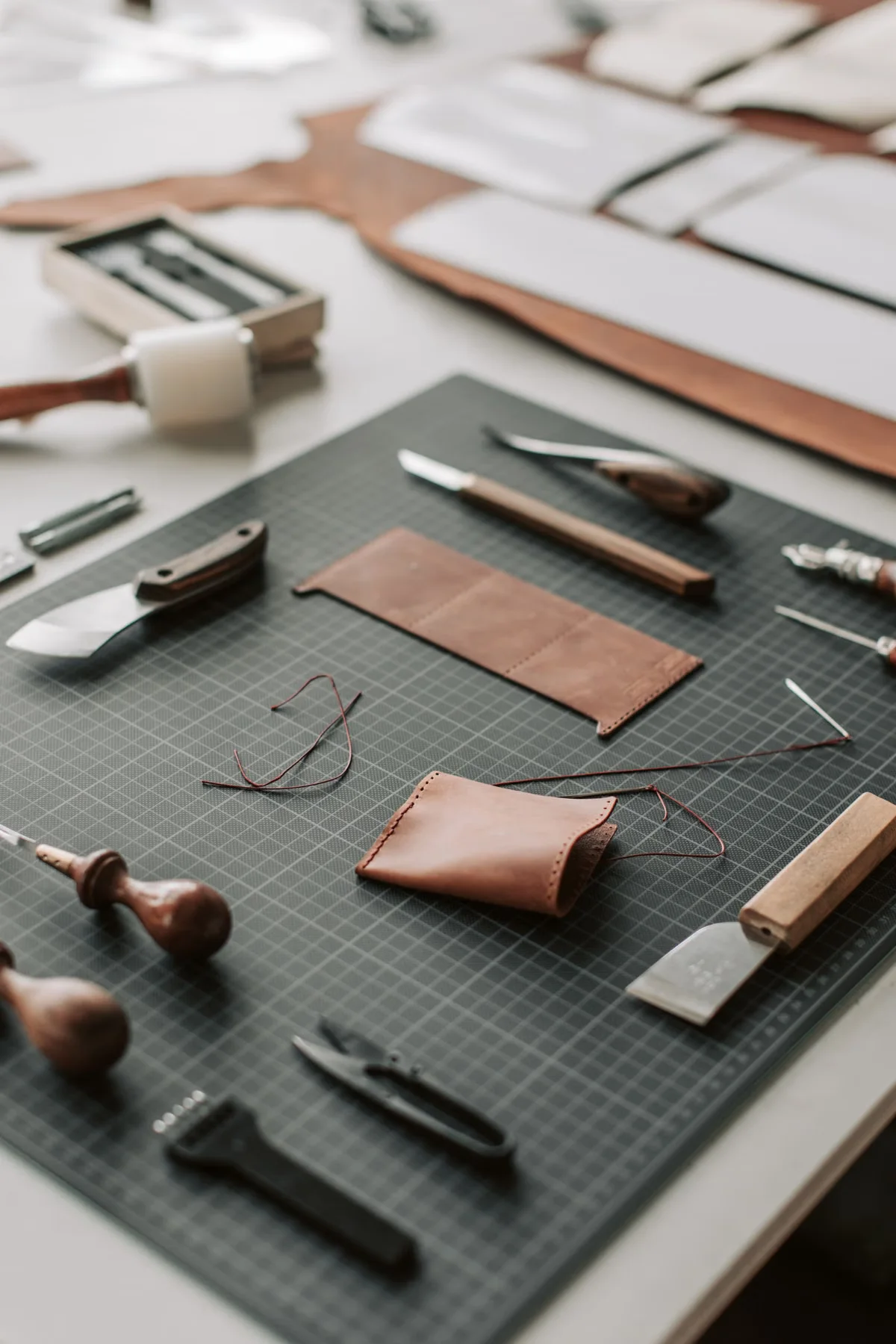 Leather craftsman workshop tools laid out for bag pattern cutting and stitching — the specialized equipment used to assess and work full-grain and top-grain leather in quality manufacturing
