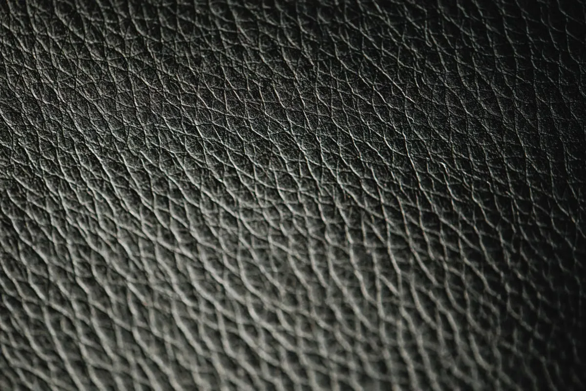 Richly textured dark leather surface with distinctive natural grain — the aged, characterful surface of well-tanned leather is the material counterpart to the intentional patina of antique brass hardware