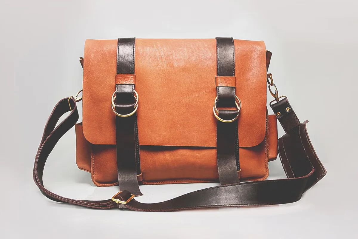 A finished brown genuine leather messenger bag displayed against a clean white background — representing the final product inspection stage before a production run is approved for shipment
