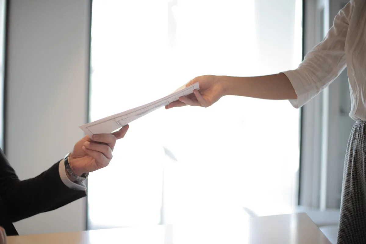 Two people exchanging documents across a table in a business context — the exchange of specifications, quotes and counter-proposals is central to the leather bag factory price negotiation process
