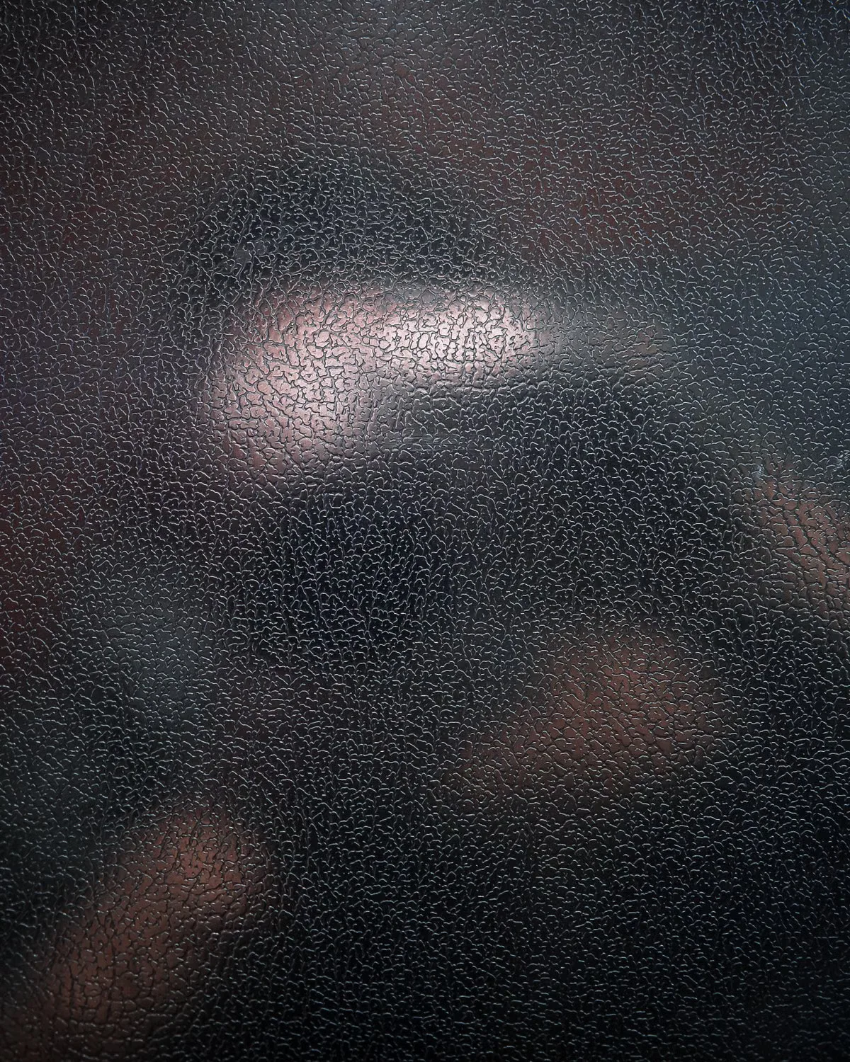 Extreme close-up of a dark pebbled leather surface showing the tight grain pattern — the kind of detail inspection that reveals whether a surface is genuine full-grain leather or a bonded or coated substitute