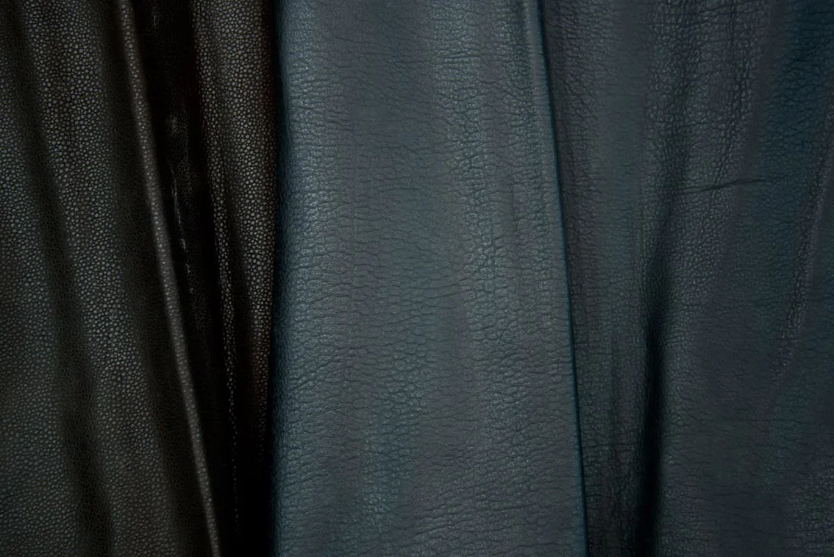 Multiple leather hides in different tannages and textures laid side by side — the variation in surface character, sheen and grain structure reflects differences in tanning method, finishing and hide selection