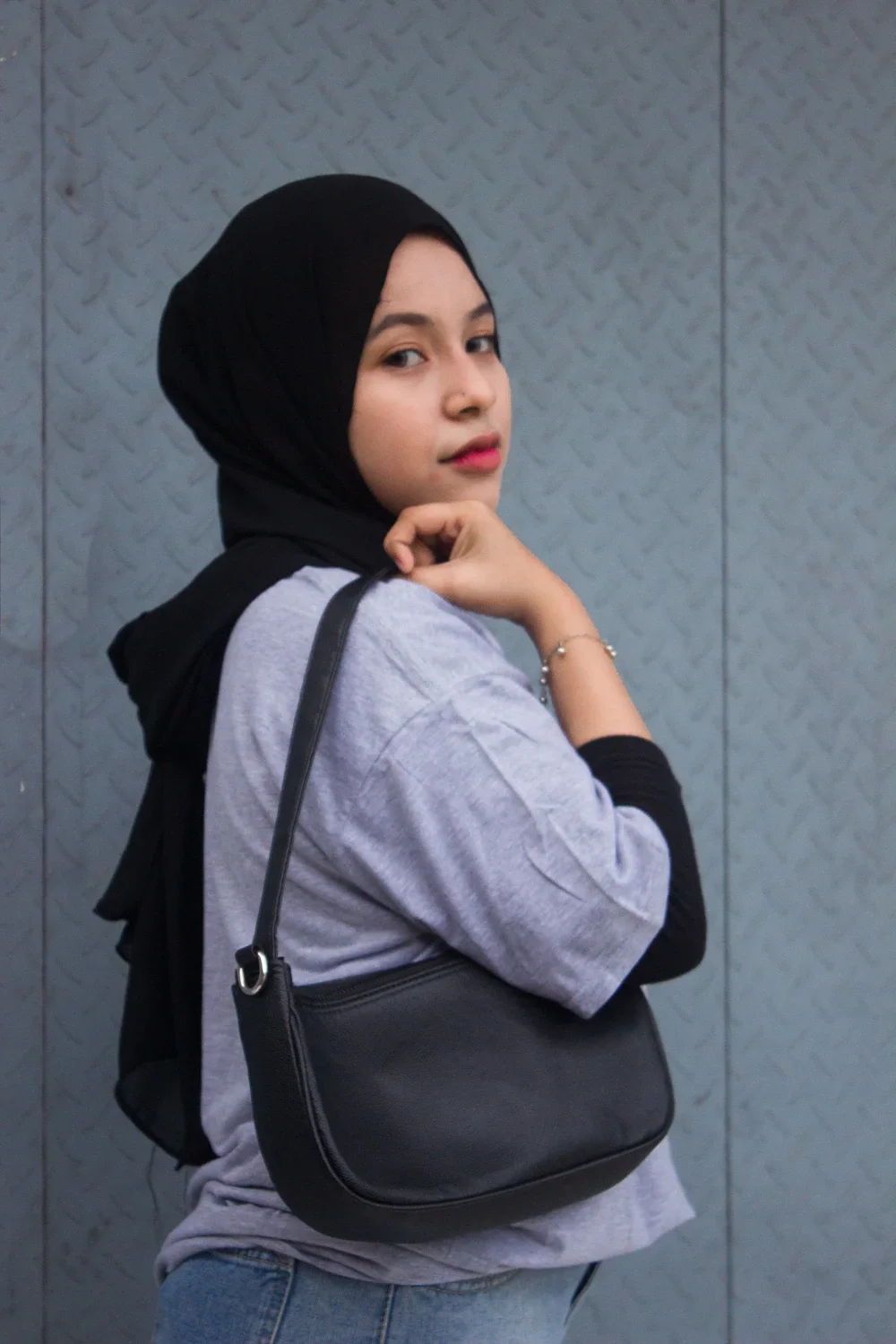 A woman wearing a black leather crescent shoulder bag — showing the natural fit against the body