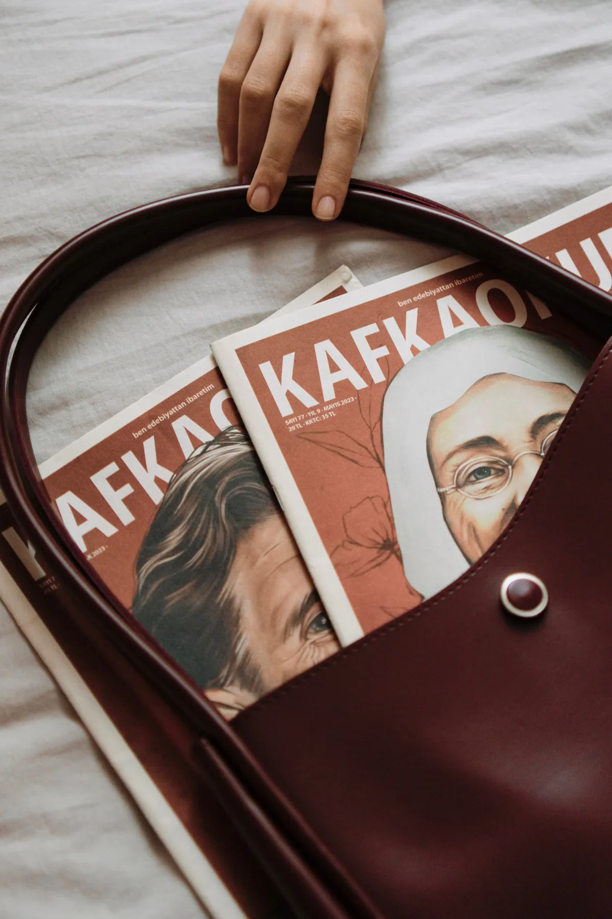 Overhead view of a dark red leather tote bag with magazines inside, showing the bag's open-top interior and its capacity to carry flat documents and printed material — illustrating the practical carrying utility of a medium tote format