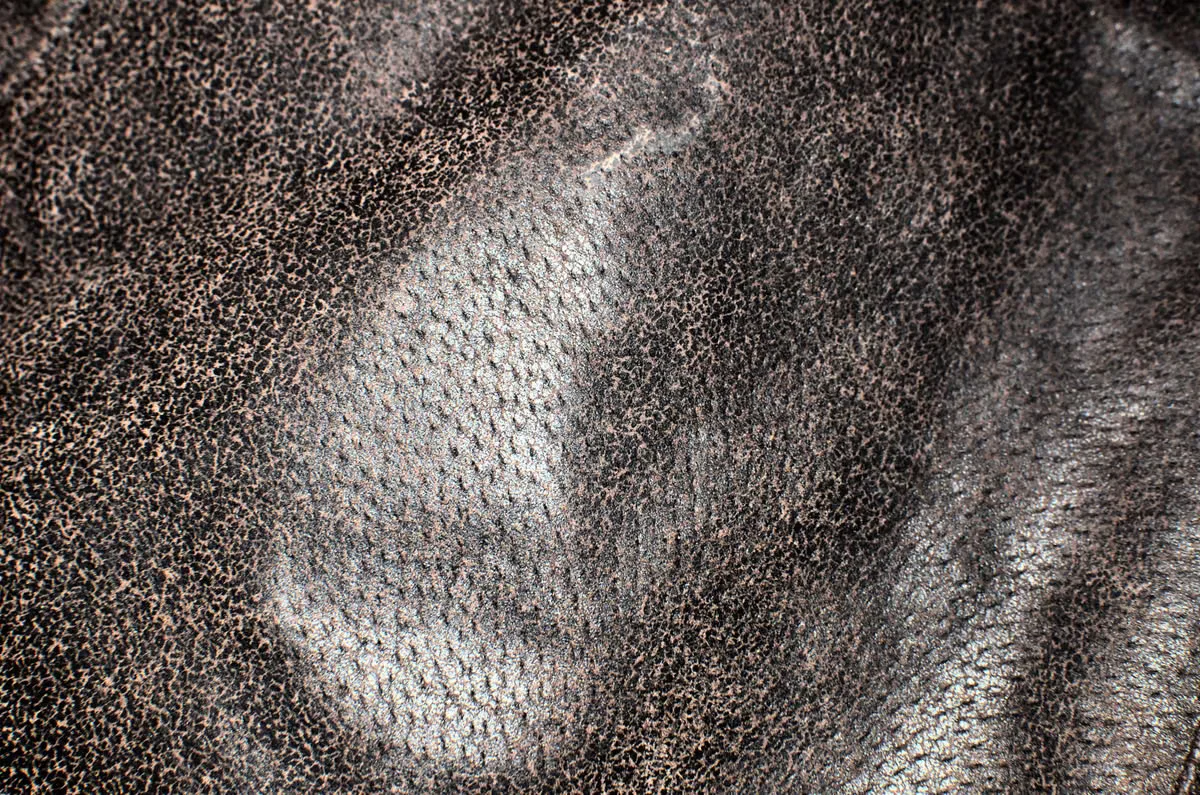 Extreme close-up of dark suede leather fabric showing the natural napped fiber structure — the biological origin and unique fiber network of genuine leather creates properties no synthetic material fully replicates in wholesale bag production